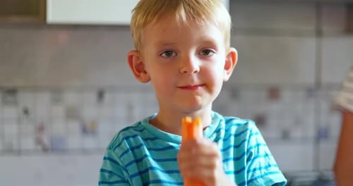 Child Eating Carrot Stick in Kitchen