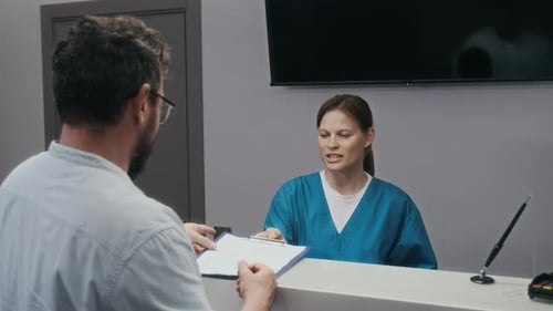 Man Signing Healthcare Form at Hospital Reception Desk