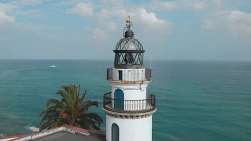 Close clockwise aerial shot of lighthouse on the coast with the ocean in the background in Catalonia