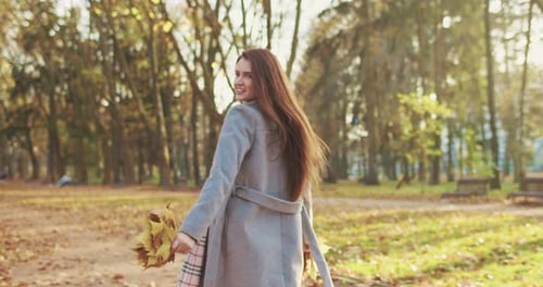 Rear of Stylish Caucasian Brunette Woman with Long Hair and in Coat Walking in Park on Autumn Day