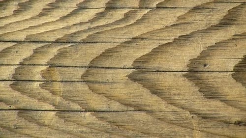 Plan rapproché d'une planche de bois rustique présentant des fissures et un grain de bois proéminent.