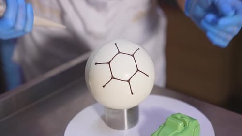 Confectioner decorates ball-shaped white cake with chocolate. Producing desserts at factory