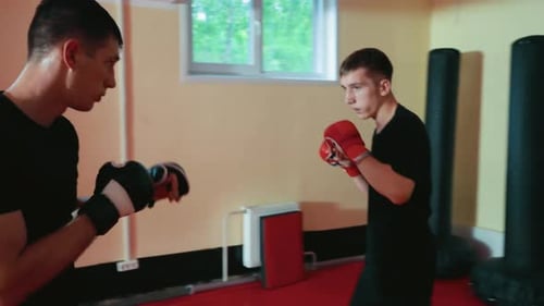 Luchadores entrenando en el gimnasio, un joven con guantes rojos se enfrenta a un oponente