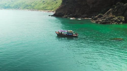 Traditional Fishing Boat Sailing Near Green Rocky Coastline Cutting Through Tranquil Turquoise