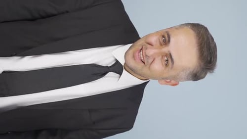Smiling Man in Black Suit Gesturing in Studio