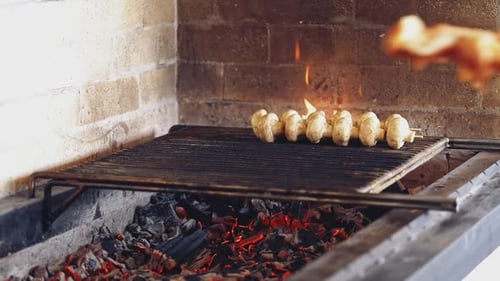 Cooking mushrooms on grill. Cook puts some skewers with chicken meat on charcoal.