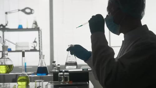 Dark Silhouette of a Male Scientist Conducting a Scientific Experiment A Man Using a Pipette Will