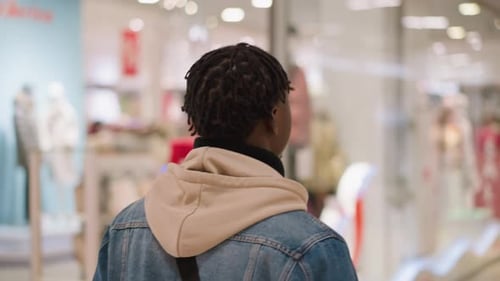 Young Black Man Browsing Denim Jacket in Shopping Mall Interior