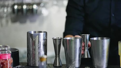 Metal cups and beavers used for making cocktails in the bar. Male in black shirt fills the metal jar