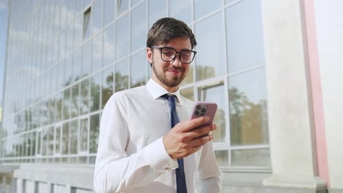 Professional Man Using Smartphone Outside a Modern Office Building During Bright Daytime
