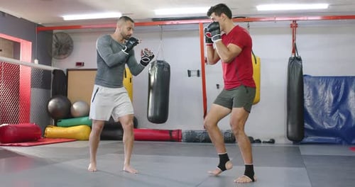 Vielfältiges männliches Trainingsduo reagiert auf einen abstoßenden Schlag und übt Beinarbeit auf einer Gymnastikmatte, um die Entfernung zu sondieren