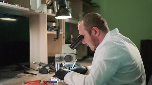Technician Examining Electronic Component Under Microscope