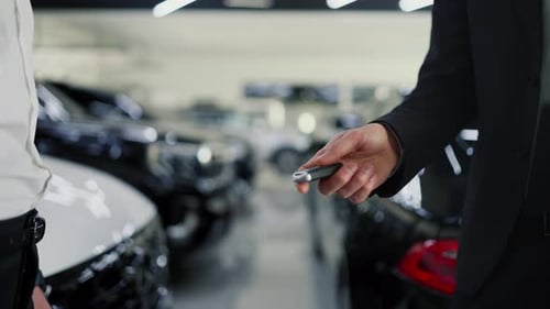 Asistente masculino seguro de sí mismo con un traje blanco y negro que entrega las llaves del auto a un hombre feliz en un