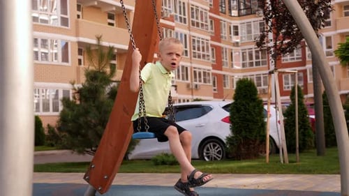 A Little Happy Boy Rides on a Swing on a Modern Playground in the Courtyard
