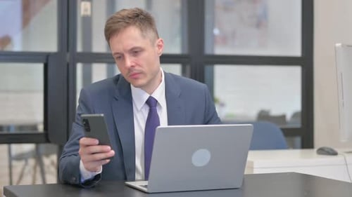Man Using Phone at Laptop in Office