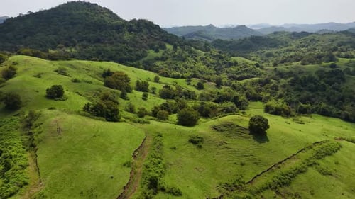 Drone flying over green hills with mountains in the background in