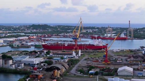 Industrial seaport cranes above tanker transit ship docked in port at sunset on island