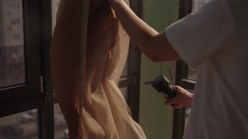 Person Steaming Clothing Near Window in City Apartment