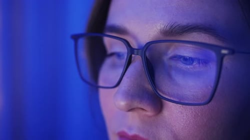Woman in Glasses Concentrating with Blue Light Reflection