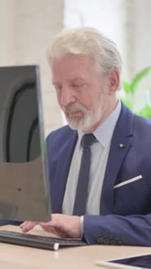 Older Man Types at Computer and Looks at Camera