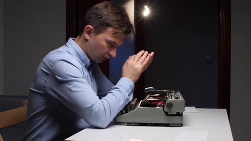 Man Frustrated at Typewriter in Dimly Lit Room