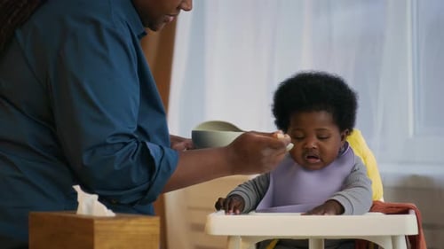 Parent Feeds Smiling Infant in High Chair