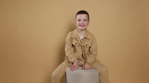 Smiling Boy Sits on a Stool Against Neutral Backdrop