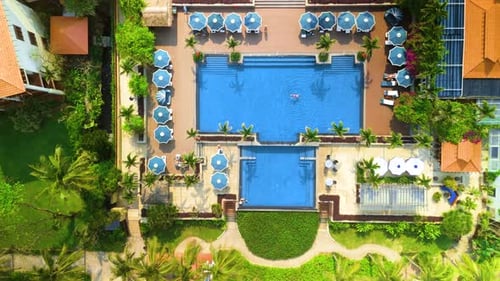 Aerial View of a Luxurious Tropical Resort Swimming Pool with Blue Umbrellas Palm Trees and Lush