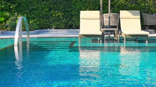 Zwei Liegestühle unter einem Sonnenschirm am Pool in einem tropischen Resort mit üppigem Hintergrund
