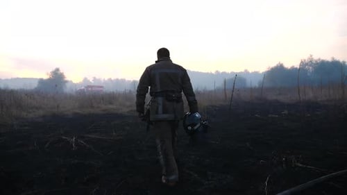 Firefighter Walks Through Scorched Field in Smoky Landscape