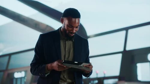 A cheerful businessman awaits his flight at the airport, holding a tablet