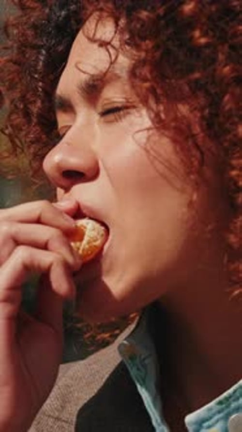 Vertical video, Young Woman Eating a Mandarin Orange Outdoors