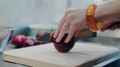 A skilled female chef slices a vibrant beetroot on a clean cutting board in her kitchen.