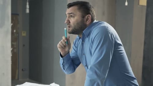 Thoughtful Engineer Reviews Building Blueprint Plans Indoors