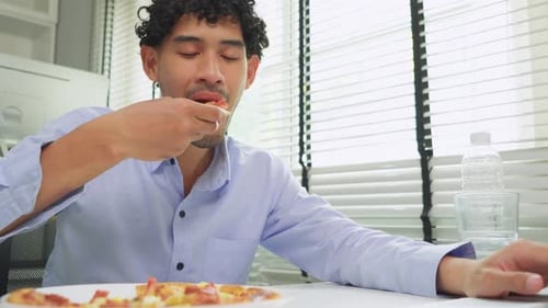 Asian young businessman eating homemade pizza while working in office.