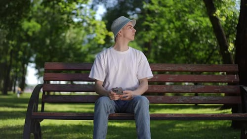 A Guy in a Sun Hat is Nervous and Fussily Looking at the Screen of a Mobile Phone in His Hands While