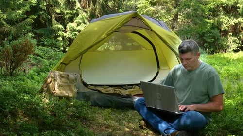 A Man Works on a Laptop in a Tourist Camp in a Beautiful Forest