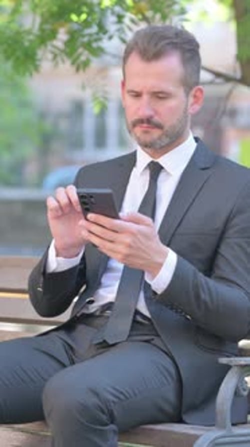 Man in Suit Using Phone on Park Bench