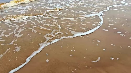 The ocean is calm and the waves are small. The water is brown and the sand is light brown