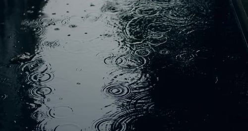 Closeup of Drizzling Torrential Rain Hitting a Puddle During a Suburban Storm