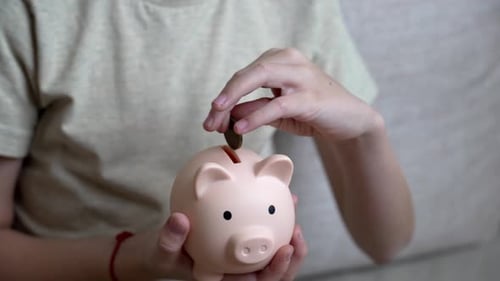 Child saving money putting coins in piggy bank