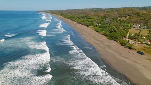 Long sandy coastline with blue ocean waves rolling toward lush tropical shore