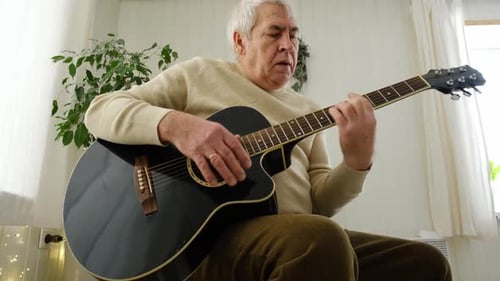 Senior Man Plays Acoustic Guitar in Bright Room