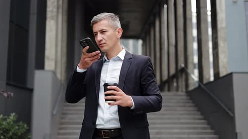 Businessman Talking on Speakerphone Holding Coffee Outside Office