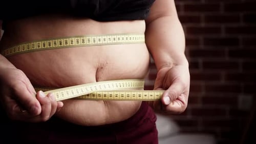 Hands of Stout Woman Tighten Huge Belly with Yellow Measuring Tape Closeup