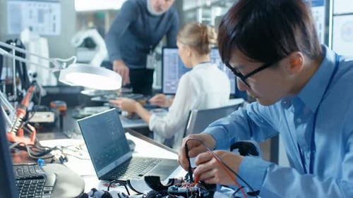 Electronics Engineer Works with Robot, Manipulating its Responses and Checking Data with Laptop Com