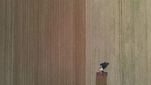 An aerial view of a tractor working on a large agricultural field, plowing the soil in straight, par