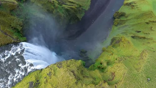 Skogafoss waterfall in the springtime. Vibrant green grass. Slow motion aerial view