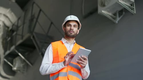 Professional engineer wearing safety helmet and vest standing at the factory and working