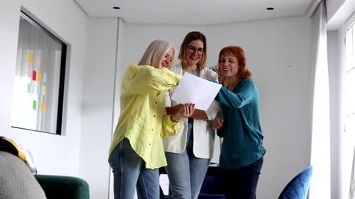 Three businesswomen stand together, carefully reviewing and discussing a document, sharing their tho